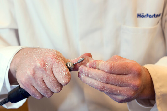 Ein Hörakustiker schleift ein Ohrpassstück für ein individuelles Hörgerät zurecht.